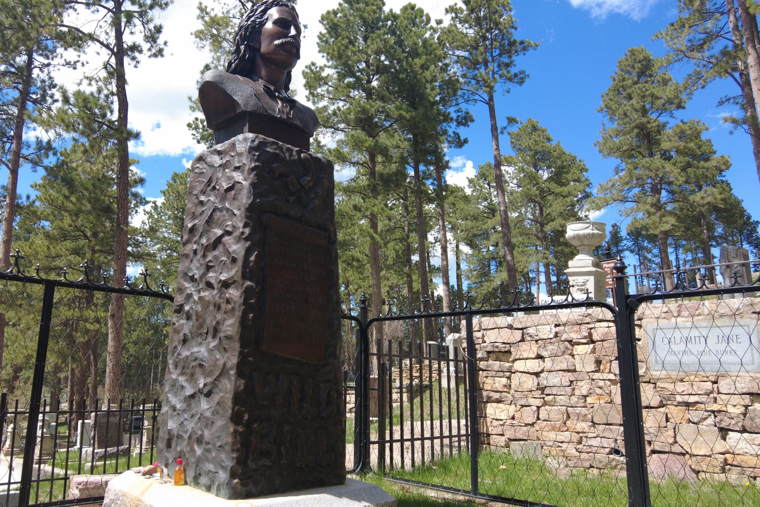 a gravesite with a bust of Wild Bill Hickock and a plaque marking Calamity Jane's grave